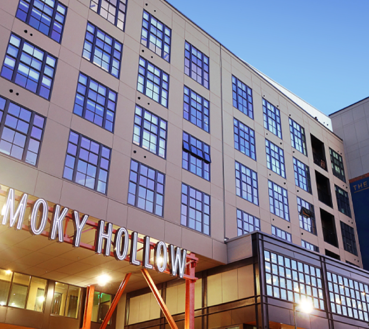 Multi-story brick building with regular grid of blue-tinted windows and illuminated ground-level storefront.