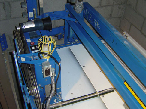 Blue industrial 3D printer with white build platform and mechanical components mounted on frame.