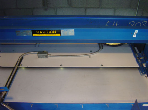 Blue industrial machinery with caution label, metal framework, and mechanical cable system visible from above.