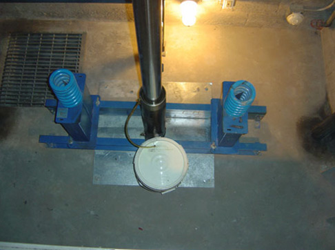 Blue industrial machinery with a white circular component and black pipe mounted on a metal base in a concrete basement.