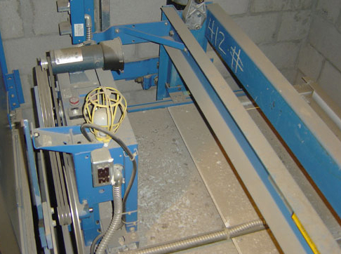 Blue industrial machinery with metal components and control panels in a concrete room.