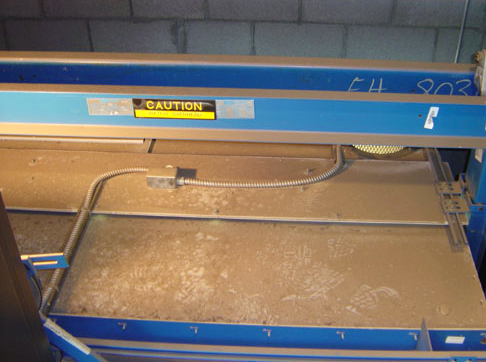 Blue industrial machine with metal work surface and yellow caution label, viewed from above.