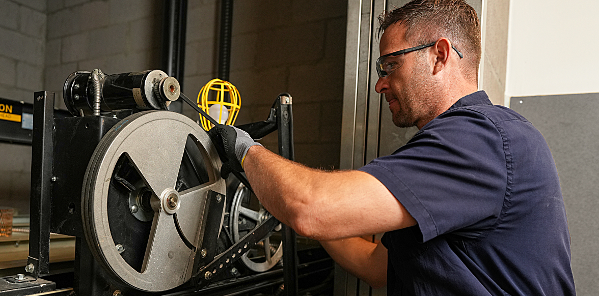 Technician in safety glasses adjusting a large pulley wheel mechanism on industrial equipment.