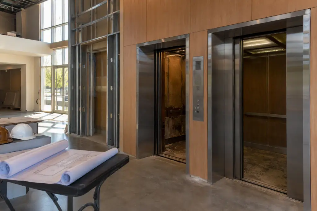 Hotel lobby elevator bank in Columbia SC during a building change-of-use renovation, with construction materials and architectural drawings visible nearby