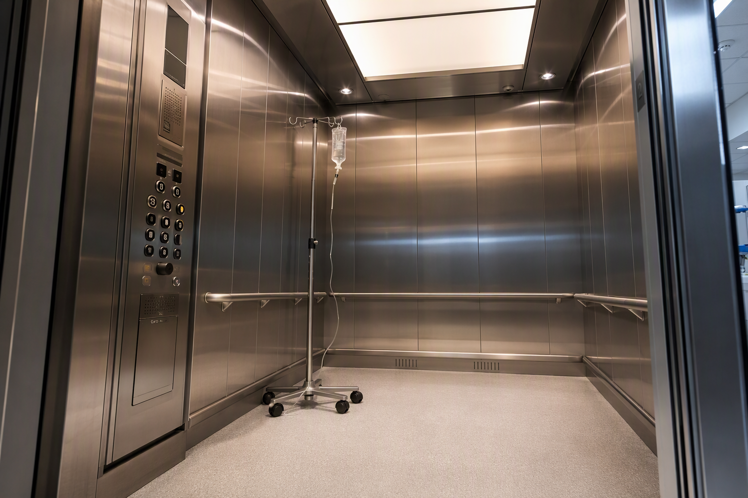 Hospital Elevator Cab Interior Detail Interior of a hospital-depth elevator cab showing stainless steel panels, antimicrobial handrails, oversized ADA-compliant control buttons, and IV pole bracket